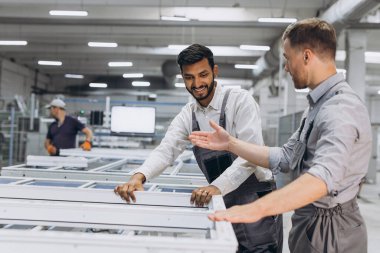 İki erkek uluslararası işçi alüminyum PVC pencere ve kapı üretimi için bir makinede birlikte çalışıyorlar.