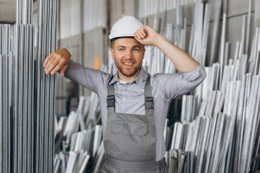 Özel üniformalı, beyaz şapkalı, sakallı, erkek fabrika işçisi metal pencere ve kapılarda alüminyum çerçeve taşıyor.