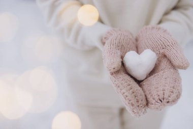 Örgü eldivenler takan kadın elleri, kışın arka planda bir kardan kalp tutar.