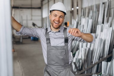 Gri üniformalı mutlu bir işçinin portresi ve fabrika yapımının arka planında poz veren beyaz bir şapka.
