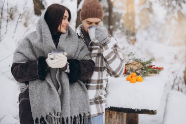 Mutlu çift dinleniyor ve ormanda sıcak çay içiyor. Kışın dağlarda.