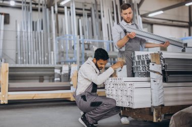 İki dikkatli uluslararası işçi kapalı atölyede pencereleri panjurla kontrol ediyor.