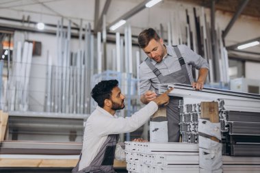 İki dikkatli uluslararası işçi kapalı atölyede pencereleri panjurla kontrol ediyor.