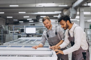 İki erkek uluslararası işçi alüminyum PVC pencere ve kapı üretimi için bir makinede birlikte çalışıyorlar.