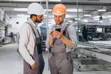 Alüminyum PVC pencere ve kapı üretiminin arka planında telefona bakan iki uluslararası erkek işçi.
