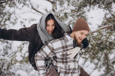 Genç ve mutlu bir çift kışın karlı bir ormanda eğleniyor..