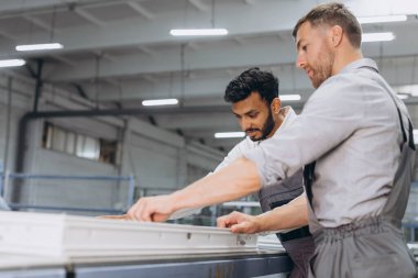 İki erkek uluslararası işçi alüminyum PVC pencere ve kapı üretimi için bir makinede birlikte çalışıyorlar.