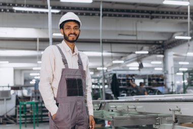 Makine operatörü. Endüstriyel Hintli uluslararası işçi fabrikada çalışıyor. Beyaz şapkalı genç teknisyen..
