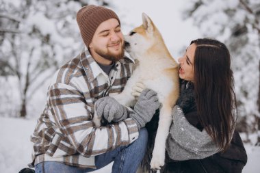 Kışın ve karlı bir günde ormanda akita köpeğiyle mutlu genç bir çift. Komik bir köpek efendinin kulağını yalar..