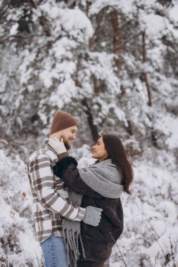 Dağlarda karlı bir ormanda yürüyen mutlu ve sevgi dolu genç bir çift.