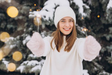 Açık havada beyaz örgü şapka, atkı, eldiven ve maytaplı süveter giyen gülümseyen kızın portresi. Noel tatili