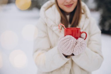 Örgü eldivenli, sevimli, mutlu bir kadın. Kış parkında elinde baston şekerlerle sıcak kahve tutuyor.