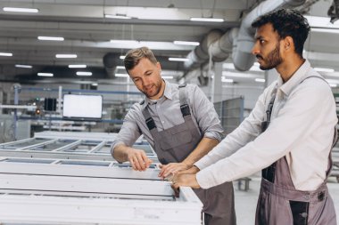 İki erkek uluslararası işçi alüminyum PVC pencere ve kapı üretimi için bir makinede birlikte çalışıyorlar.