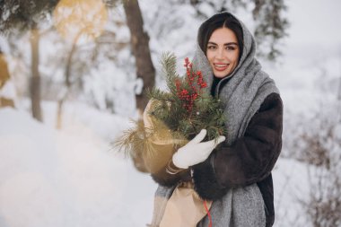 Kışın karlı ormanda elinde çam ağacı buketi tutan mutlu, güzel bir kadın..