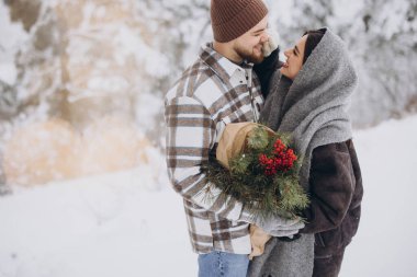 Çam buketine aşık sevimli genç çift Sevgililer Günü 'nde dağlardaki karlı kış ormanlarında vakit geçiriyor.
