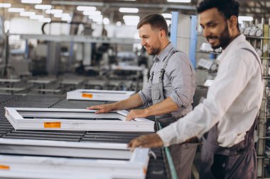 İki erkek uluslararası işçi alüminyum PVC pencere ve kapı üretimi için bir makinede birlikte çalışıyorlar.