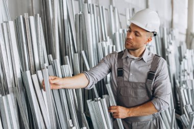 Özel üniformalı, beyaz şapkalı, sakallı, erkek fabrika işçisi metal pencere ve kapılarda alüminyum çerçeve taşıyor.