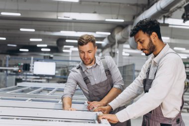 İki erkek uluslararası işçi alüminyum PVC pencere ve kapı üretimi için bir makinede birlikte çalışıyorlar.