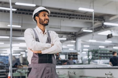 Makine operatörü. Endüstriyel Hintli uluslararası işçi fabrikada çalışıyor. Beyaz şapkalı genç teknisyen..