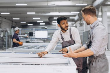 İki erkek uluslararası işçi alüminyum PVC pencere ve kapı üretimi için bir makinede birlikte çalışıyorlar.