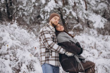Dağlarda karlı bir ormanda yürüyen mutlu ve sevgi dolu genç bir çift.