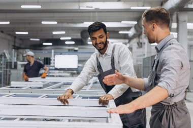 İki erkek uluslararası işçi alüminyum PVC pencere ve kapı üretimi için bir makinede birlikte çalışıyorlar.