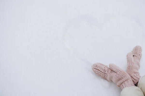 Female hands near a heart drawn on snow in winter