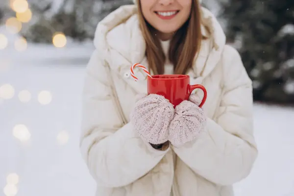 冬の公園でキャンディー缶とホットコーヒーを保持するニットミトンでかわいい幸せな女性 — ストック写真