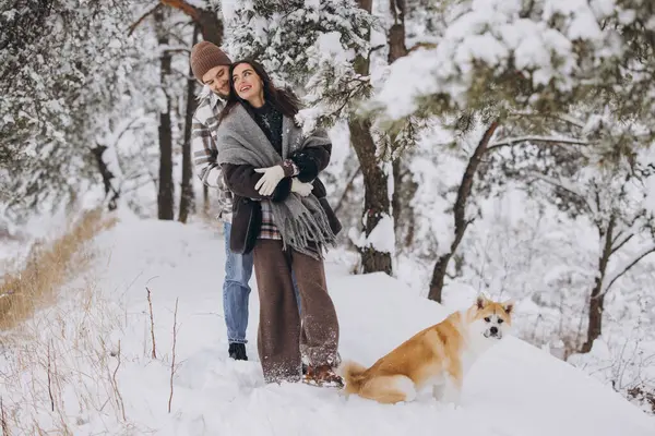 Happy young couple walking with akita dog in forest on winter and snowly day
