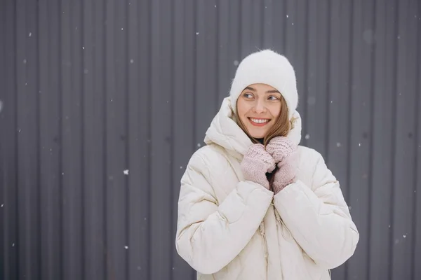 在一场大雪中 一个戴着针织手套的快乐女人在灰色的墙壁后面摆出姿势 — 图库照片