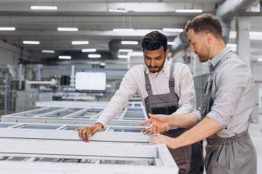 İki erkek uluslararası işçi alüminyum PVC pencere ve kapı üretimi için bir makinede birlikte çalışıyorlar.