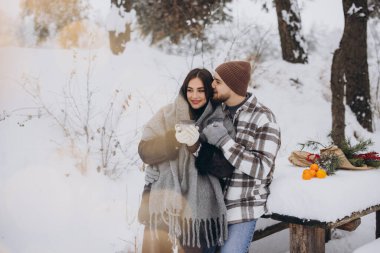 Mutlu çift dinleniyor ve ormanda sıcak çay içiyor. Kışın dağlarda.