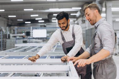 İki erkek uluslararası işçi alüminyum PVC pencere ve kapı üretimi için bir makinede birlikte çalışıyorlar.