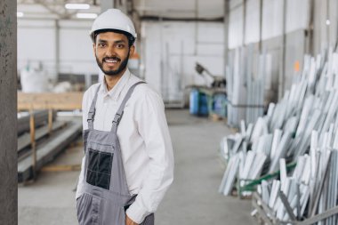 Gri üniformalı mutlu bir Hintli işçinin portresi ve fabrika yapımının arka planında poz veren beyaz bir şapka.