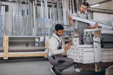 İki dikkatli uluslararası işçi kapalı atölyede pencereleri panjurla kontrol ediyor.