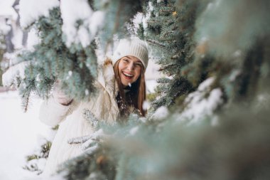 Karlı bir günde kışlık ceketle poz veren beyaz örgü elbiseli mutlu bir kızın portresi.