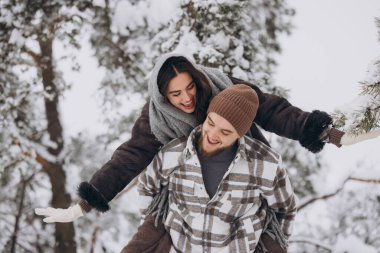 Genç ve mutlu bir çift kışın karlı bir ormanda eğleniyor..