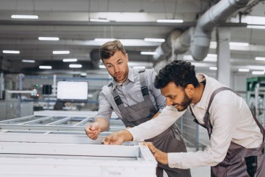 İki erkek uluslararası işçi alüminyum PVC pencere ve kapı üretimi için bir makinede birlikte çalışıyorlar.