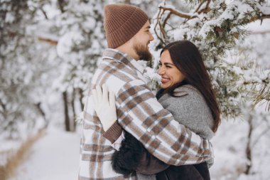 Genç, mutlu ve sevgi dolu bir çift, kışın dağlara kar yağan bir çam ağacının altında duruyor..