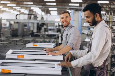 İki erkek uluslararası işçi alüminyum PVC pencere ve kapı üretimi için bir makinede birlikte çalışıyorlar.