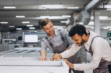 İki erkek uluslararası işçi alüminyum PVC pencere ve kapı üretimi için bir makinede birlikte çalışıyorlar.