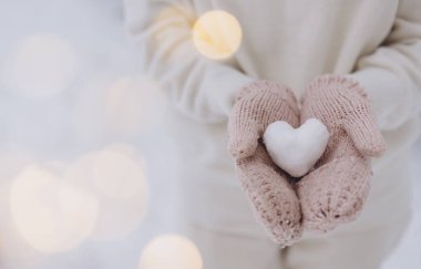 Örgü eldivenler takan kadın elleri, kışın arka planda bir kardan kalp tutar.