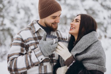 Mutlu çift dinleniyor ve ormanda sıcak çay içiyor. Kışın dağlarda.