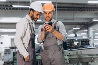 Alüminyum PVC pencere ve kapı üretiminin arka planında telefona bakan iki uluslararası erkek işçi.