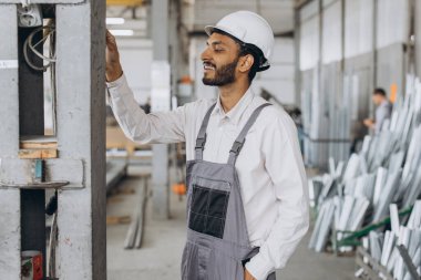 Gri üniformalı mutlu bir Hintli işçinin portresi ve fabrika yapımının arka planında poz veren beyaz bir şapka.