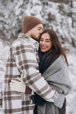 Genç, mutlu ve sevgi dolu bir çift dağlarda karlı bir ormanda yürüyor.