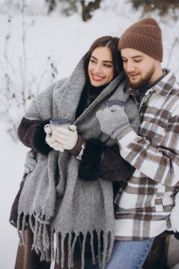 Mutlu çift dinleniyor ve ormanda sıcak çay içiyor. Kışın dağlarda.