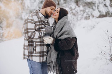 Mutlu çift dinleniyor ve ormanda sıcak çay içiyor. Kışın dağlarda.