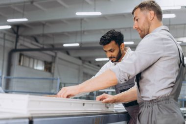 İki erkek uluslararası işçi alüminyum PVC pencere ve kapı üretimi için bir makinede birlikte çalışıyorlar.