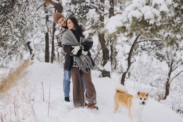 Happy young couple walking with akita dog in forest on winter and snowly day